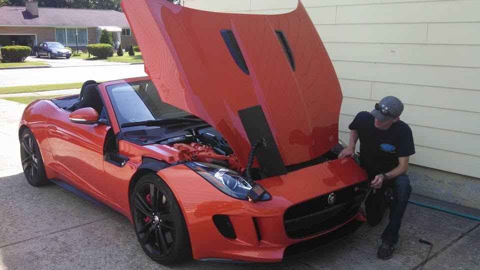 Tyler Cooper repairing a dent on the hood of an orange Jaguar F-Type convertible